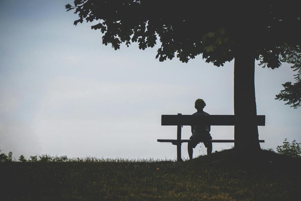 A boy seated on a bench in a mildly fleeting grey background.
